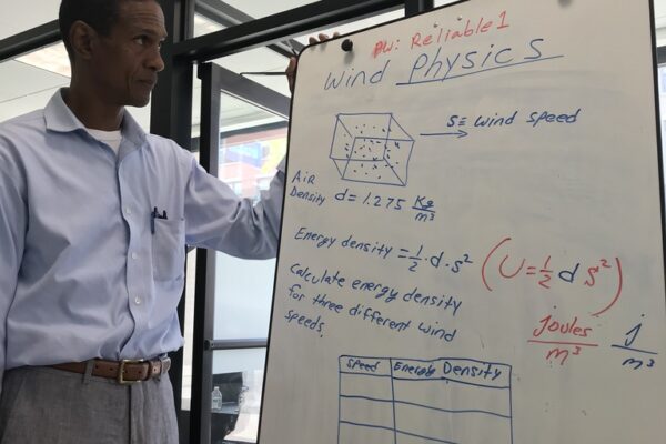 Dr. Sims standing at a whiteboard with equations and geometric shapes.